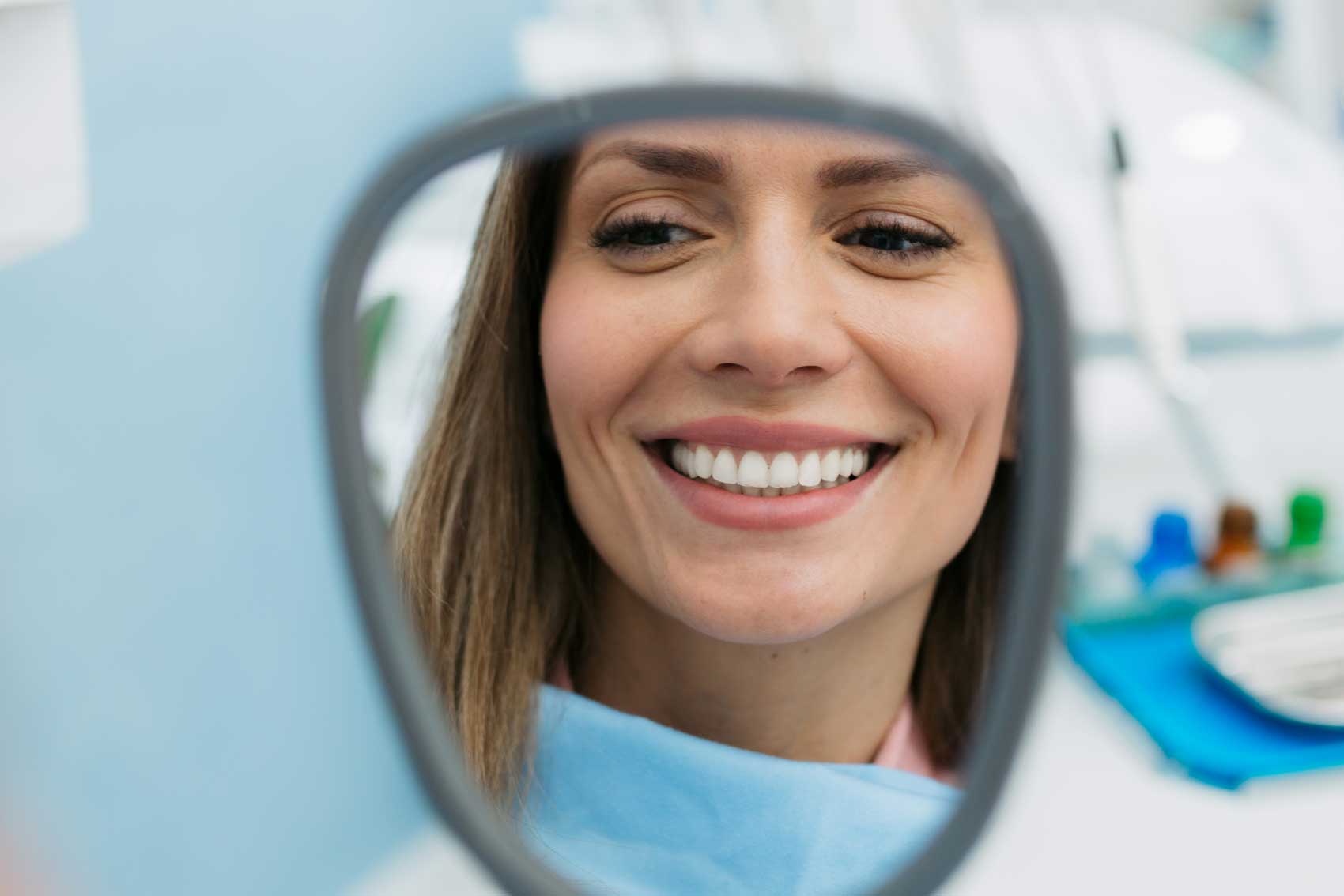Woman smiling looking at her teeth and gum in the mirror at dentist